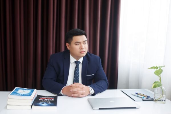 Business professional in a suit sitting at a desk with books and laptop, conveying elegance and focus.