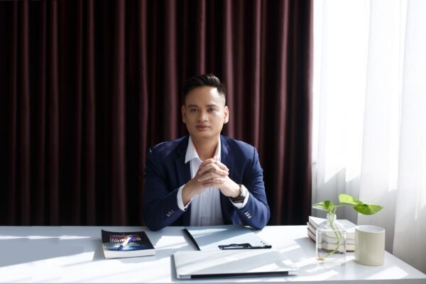 Businessman sitting confidently at a desk with a book and laptop, illuminated by natural light.