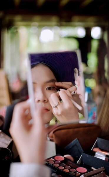 Asian woman in Ho Chi Minh City applying makeup, captured in mirror reflection.