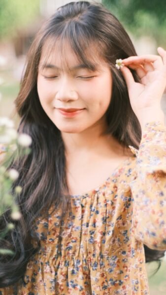 Young woman in floral dress enjoying nature with a serene expression, holding a flower.