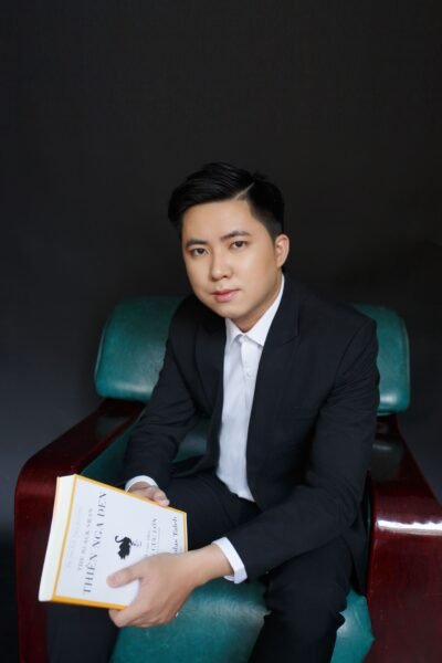 Professional portrait of a young male businessman holding a book in a chair.