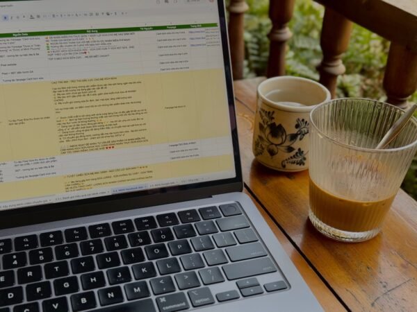 A laptop beside coffee cups on a wooden table in an outdoor setting, ideal for remote work and relaxation.