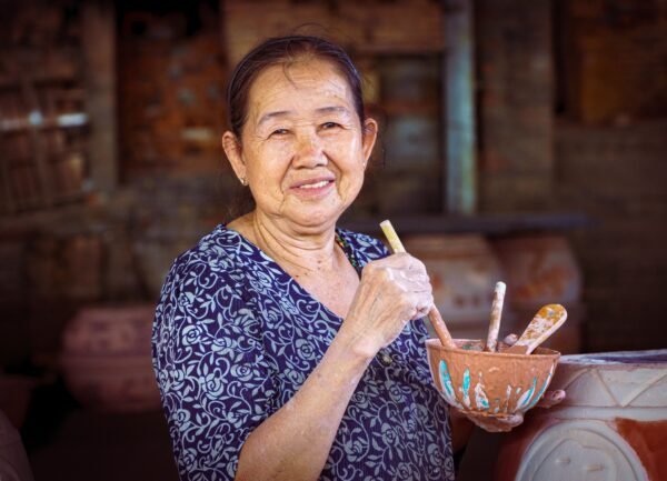 Elderly artisan creating handmade ceramics in a traditional Vietnamese pottery workshop.