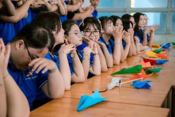 A group of students in blue uniforms preparing colorful paper planes indoors at a desk.