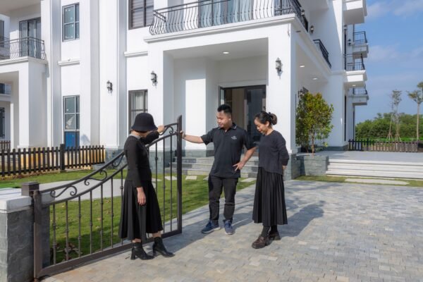 Three people interacting at the gate of a modern white house, showcasing real estate and community.