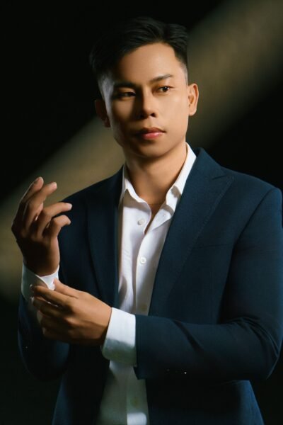Confident man in business attire posing in a studio setting with dramatic lighting.