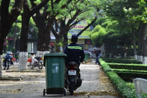 Garbage collector navigating a scenic park on a scooter, promoting urban cleanliness.
