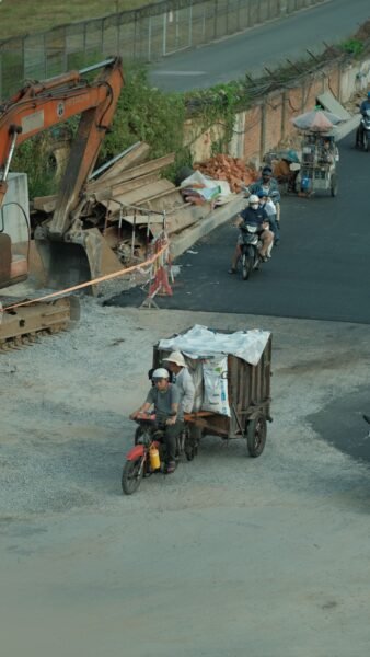 Motorcyclists passing a construction site with excavator and materials.
