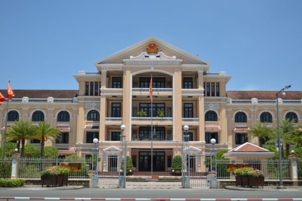 Historic colonial building with red flags in Ho Chi Minh City under clear blue sky.