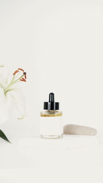 Minimalist skincare bottle and white lily on soft background, offering elegant product presentation.