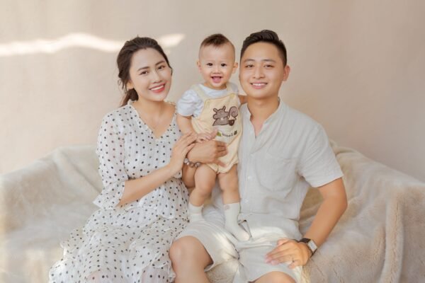 Cheerful Asian family with toddler sitting on comfortable couch and looking at camera in light room